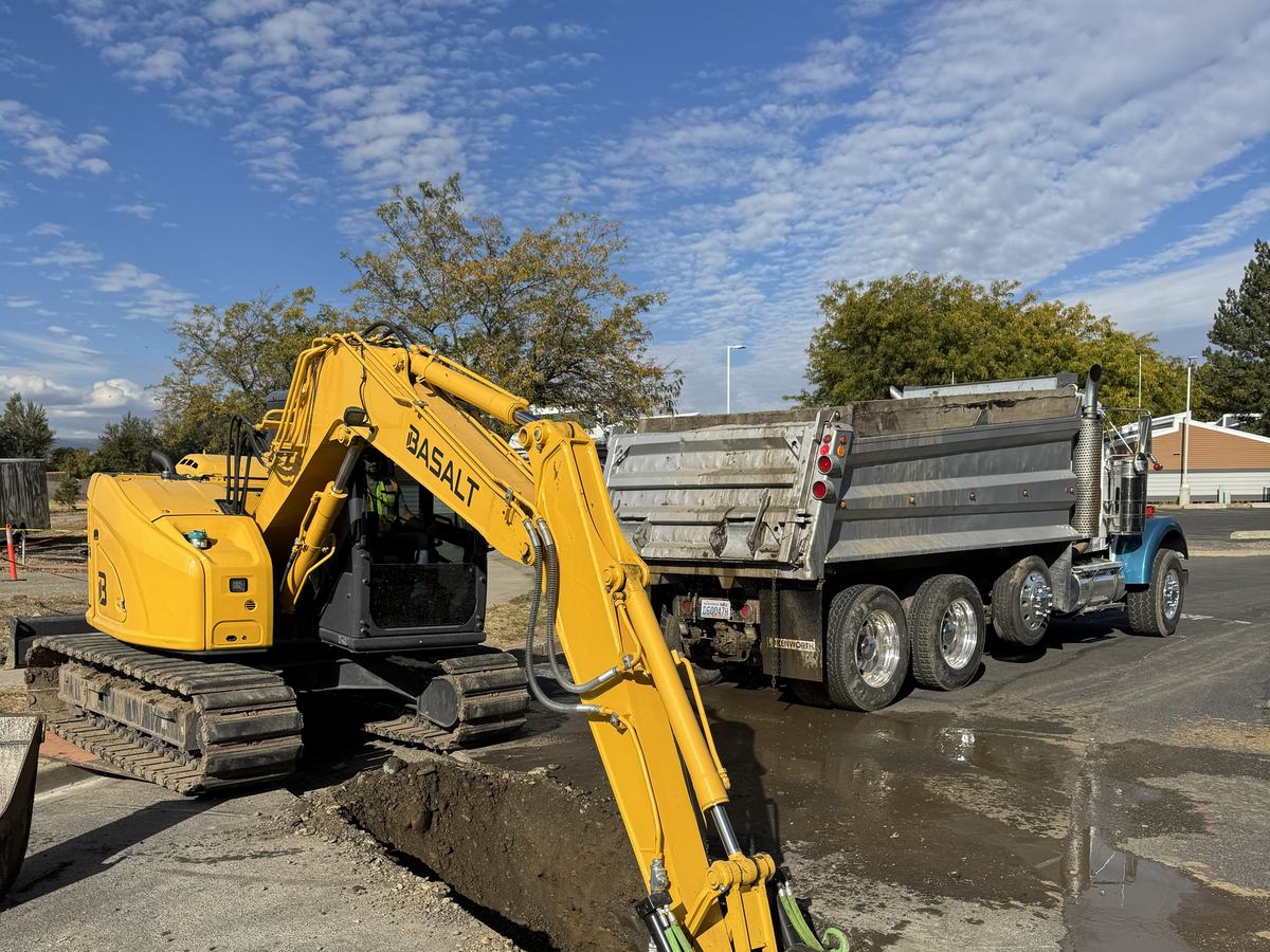 Excavator loading trench spoil into a dump truck on a city street
