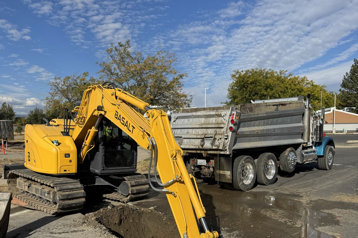 Excavator loading trench spoil into a Basalt dump truck on a wet street