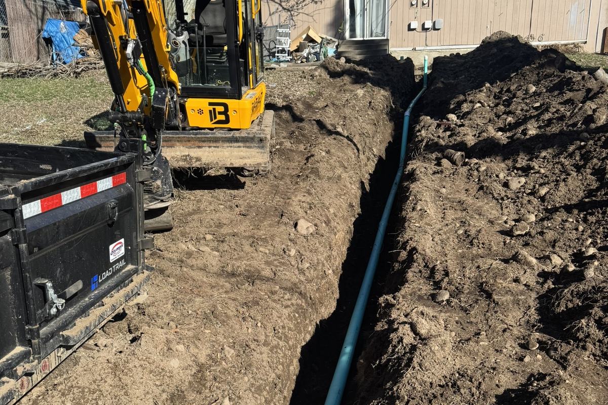 Excavator laying black HDPE pipe into an open trench