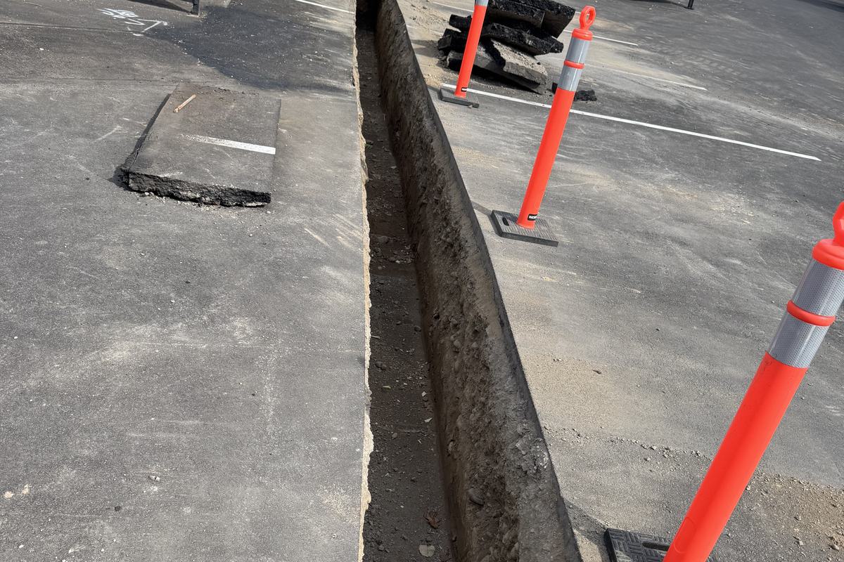 Conduit trench cut through asphalt with a steel plate and traffic cones