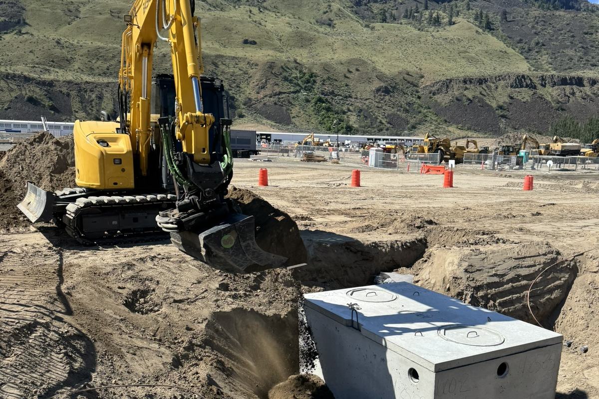 Excavator backfilling around a newly set precast septic tank